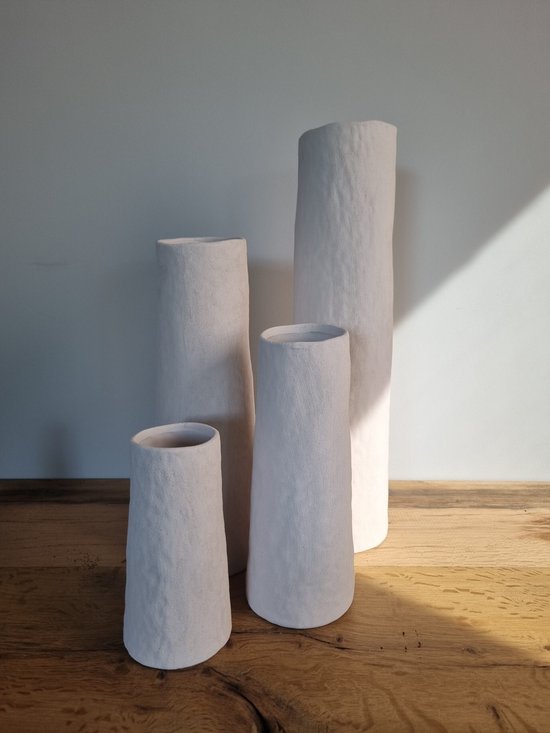 Vier witte, conische vazen met ruw, steenachtig oppervlak, opgesteld op een houten ondergrond.
