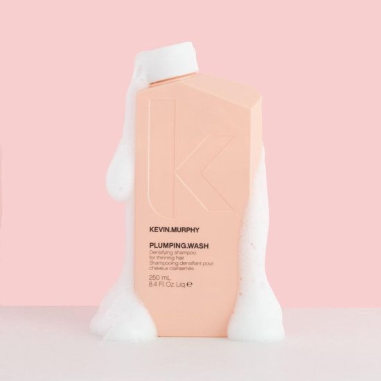 Perzikkleurige fles KEVIN.MURPHY PLUMPING.WASH shampoo omringd door schuim.