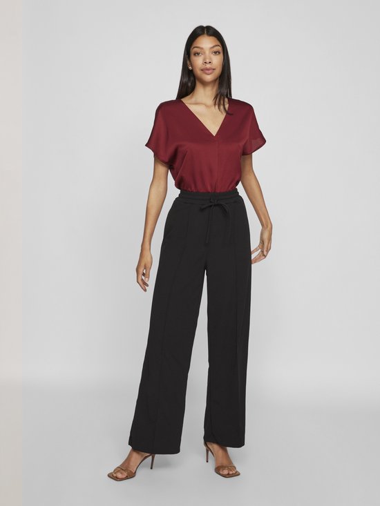 Model met bordeauxrode top met korte mouwen en V-hals, gecombineerd met een zwarte broek met hoge taille en ceintuur.