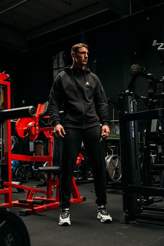 Man met spierbundel met een zwarte trainingsjas en trainingsbroek van Gorilla Wear in een sportschool.