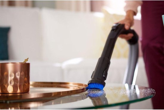 Aspirateur Philips avec brosse bleue nettoie une table en verre.