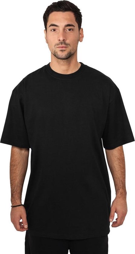 Man gekleed in een oversized zwart t-shirt en zwarte broek, staand, van voren gezien.
