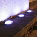 Vier roestvrijstalen grondspots met LED-verlichting, in de grond geplaatst langs een muur.