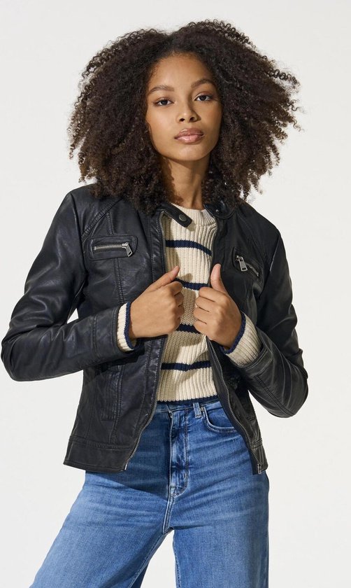 Meisje met krullend haar in een zwarte faux leren bikerjack met ritsen, een gestreepte trui en jeans.