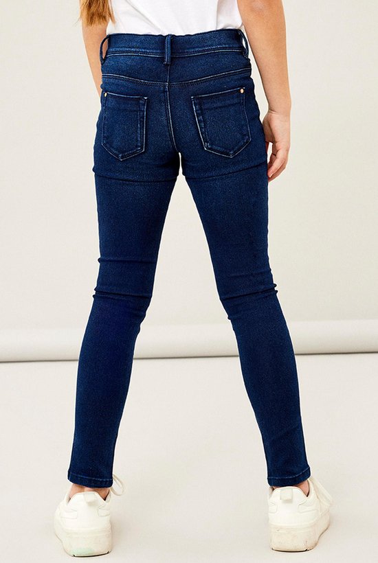 Achterkant van een meisje in een donkerblauwe skinny jeans en witte sneakers.