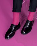 Pieds en chaussettes rose vif et chaussures habillées noires, sur fond rose.
