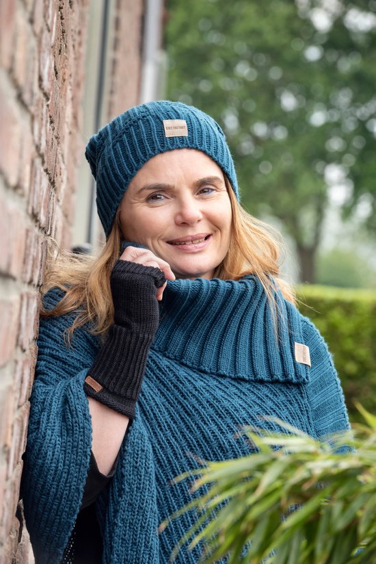 Close-up van een vrouw in een blauwe gebreide poncho met col en een 'Knit Factory' label.