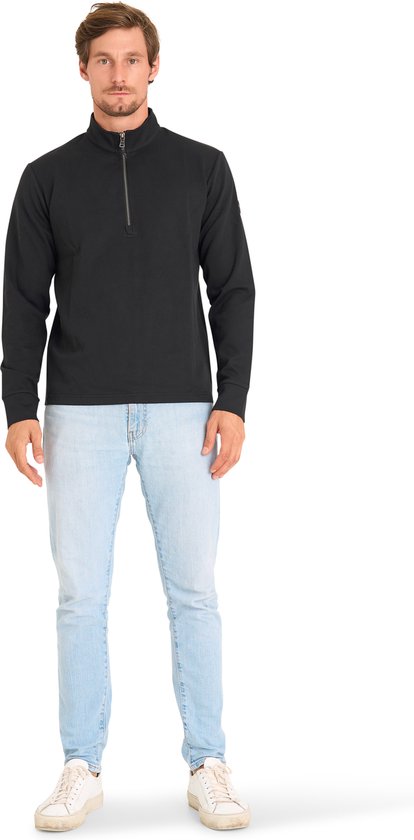 Man draagt zwarte trui met ritskraag, lichtblauwe jeans en witte sneakers, voorkant zichtbaar