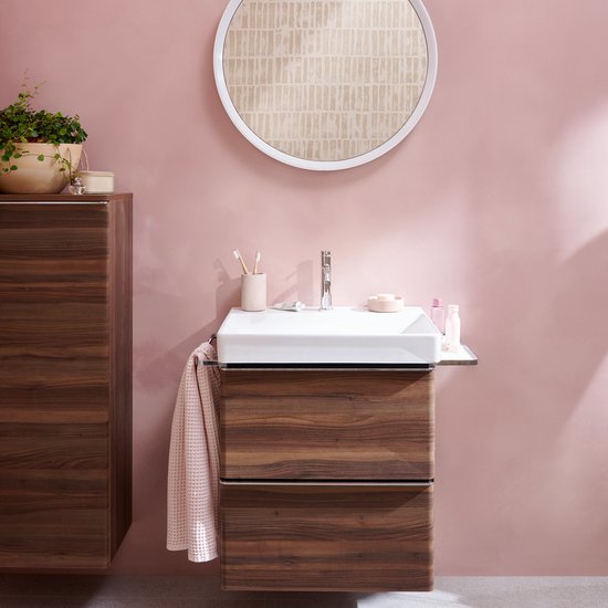 Een stijlvolle badkamer met een wastafelmeubel van donker hout, een witte wastafel, spiegel en plant.