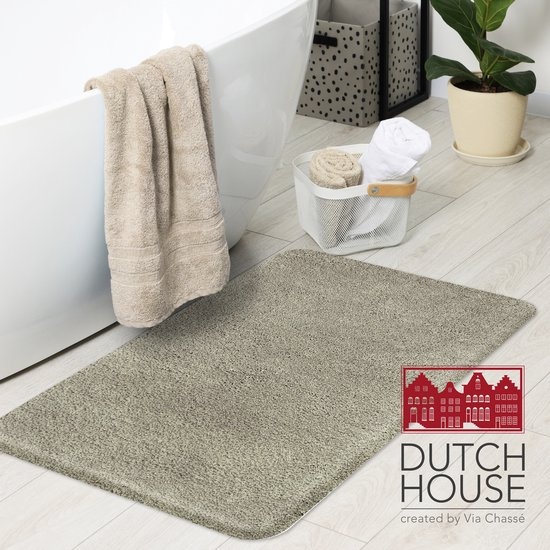 Grijze badmat van 'Dutch House' in een badkamer, naast een badkuip met handdoeken.