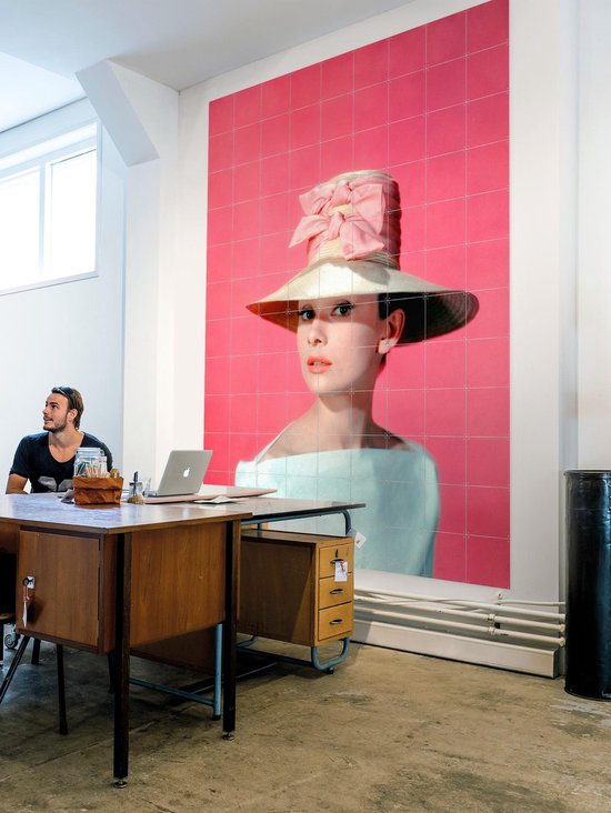 Audrey Hepburn portant un grand chapeau de paille et un nœud rose sur fond rose.