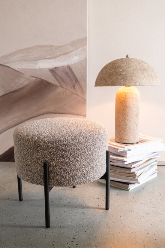Crème-kleurige bouclé kruk met zwart metalen poten, naast een stapel tijdschriften met lamp.