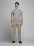 Model in een grijs T-shirt met klein logo en beige chino. De volledige voorkant is zichtbaar.