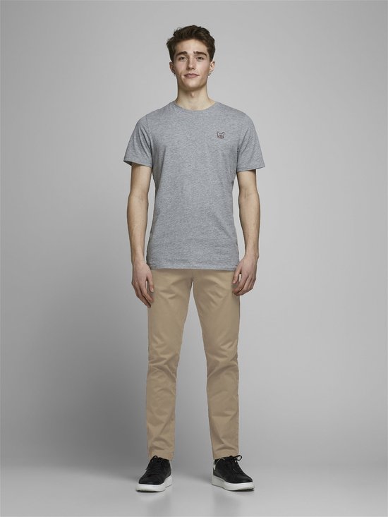 Model in een grijs T-shirt met klein logo en beige chino. De volledige voorkant is zichtbaar.