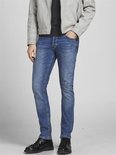 Man met de hand in de zak van een blauwe jeans, met grijze jas.