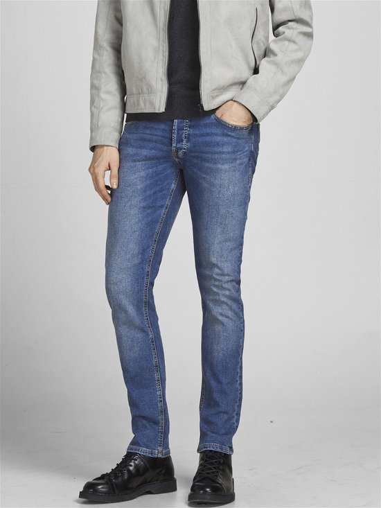 Man met de hand in de zak van een blauwe jeans, met grijze jas.
