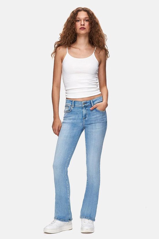 Model draagt een witte tanktop en een lichtblauwe flared jeans met riemlussen en zakken.