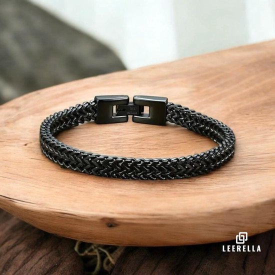 Zwarte, gevlochten armband met metalen sluiting op een houten ondergrond.