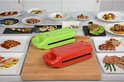 Twee elektrische grills, rood en groen, omringd door diverse borden met bereid voedsel.