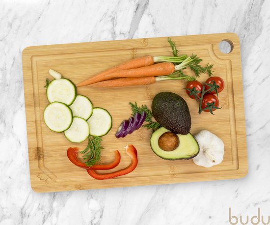 Een Budu bamboe snijplank met gesneden courgette, wortels, rode ui, avocado, knoflook, tomaatjes en rode paprika.