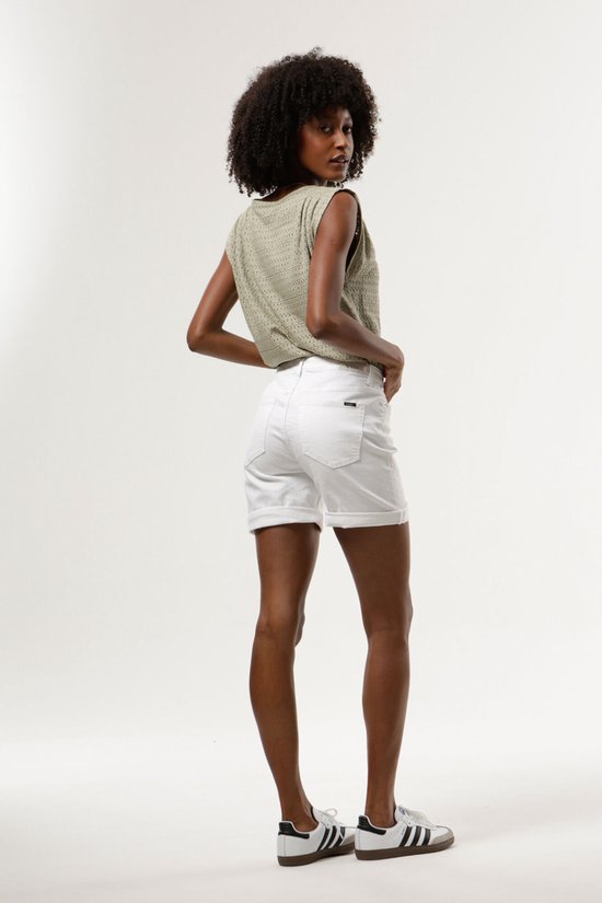 Model met donkere huid draagt een olijfgroene top en witte denim shorts met opgerolde zoom.
