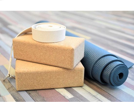 Twee kurken yogablokken en een opgerolde blauwe yogamat op een houten ondergrond. Een witte band met lus ligt bovenop de blokken.