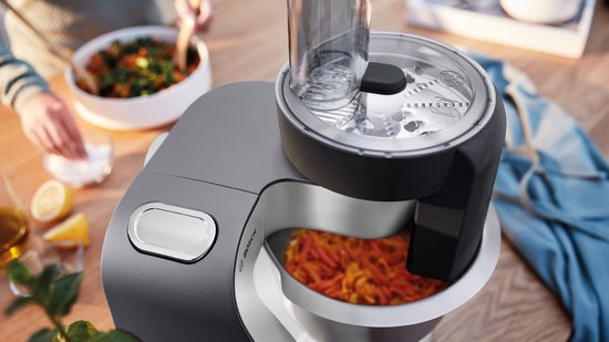 Robot de cuisine gris avec accessoire robot culinaire, coupant des carottes.
