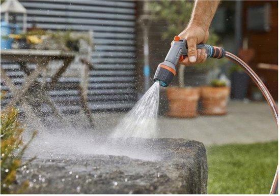 Hand sproeit een stenen steen met een Gardena spuitpistool in een tuin.