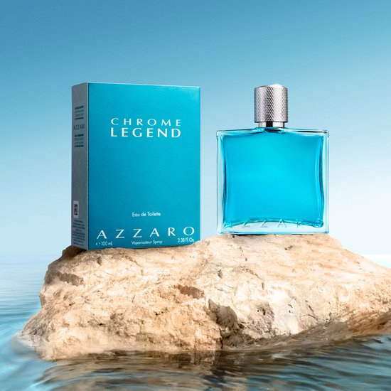 Een Azzaro Chrome Legend Eau de Toilette 100 ml fles en doos op een rots bij het water.