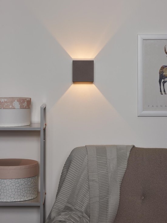 Taupekleurige kubuswandlamp aan een muur, die licht naar boven en beneden straalt.