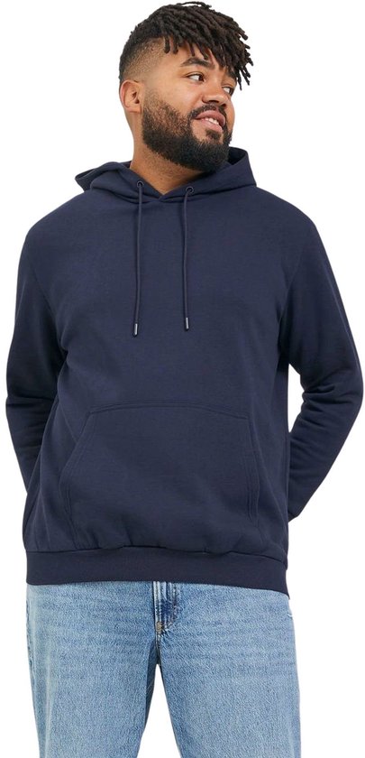 Man met dreadlocks, gekleed in een donkerblauwe hoodie met trekkoord en een grote zak aan de voorkant, met een spijkerbroek.