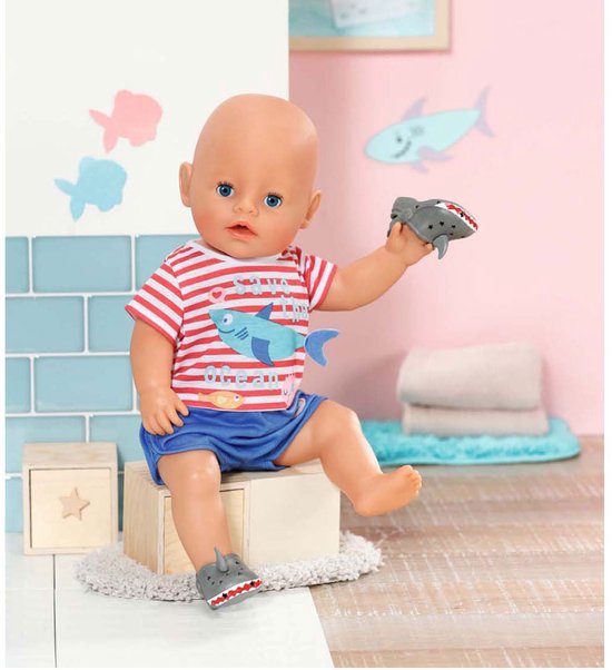 Baby Born pop zittend, met rood-wit gestreept shirt met haai en blauwe broek. Draagt grijze haaienschoentjes. Houdt een haaienschoen vast.