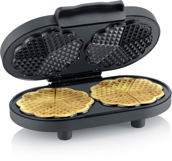 Zwart wafelijzer open met twee gebakken gouden wafels in hartvorm.