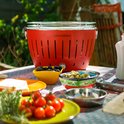 Rode LotusGrill met olijven en cherrytomaten op een tafel.