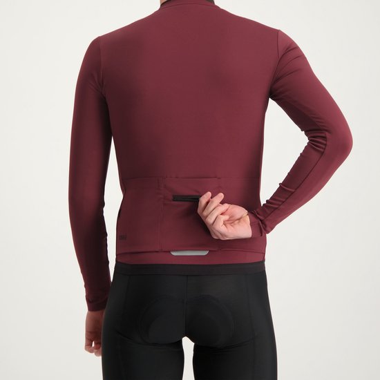 Man gebruikt de rits van de achterzak van een donkerrood wielershirt met lange mouwen. Reflecterende strip zichtbaar.