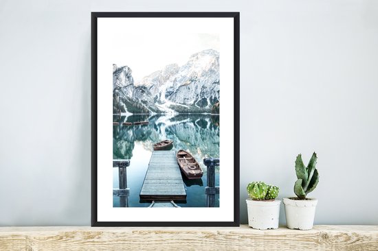 Winterlandschap met bergen, water en boten, in zwarte lijst, staand op meubel.
