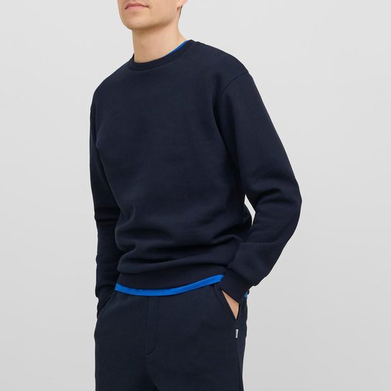 Man met donkerblauwe, effen sweater met ronde hals en blauwe rand van het shirt eronder.