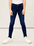 Een meisje in een donkerblauwe skinny jeans met witte sneakers.