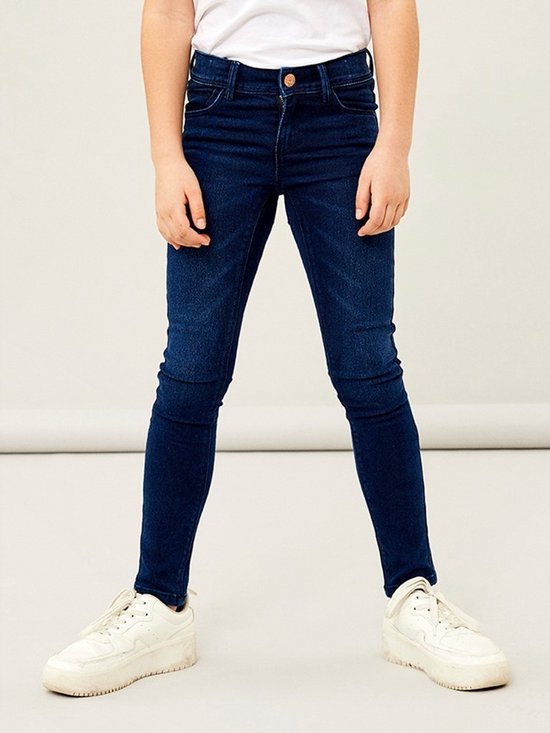 Een meisje in een donkerblauwe skinny jeans met witte sneakers.