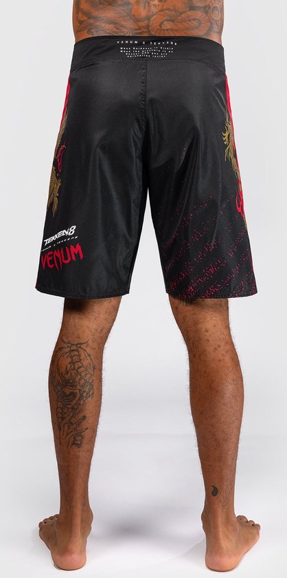 Achterkant van zwarte fightshorts met gouden drakenprint, rode streep en rode spetters. Venum logo op de tailleband.