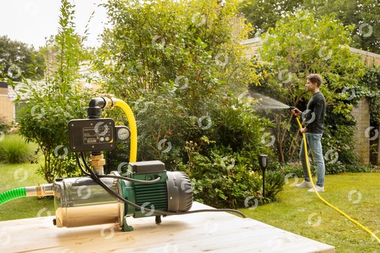 Man met tuinslang en pomp in de tuin. De pomp staat op een houten tafel.