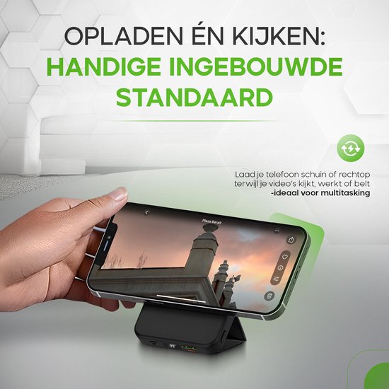 Een hand kantelt een smartphone op een zwarte powerbank met ingebouwde standaard, kijkend naar een video. Tekst: "Opladen én kijken: Handige ingebouwde standaard."