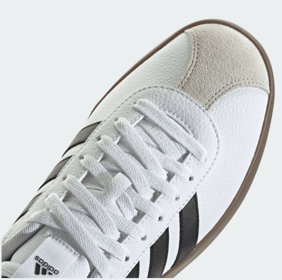 Close-up van de witte sneaker met bruine zool, zwarte strepen en Adidas logo.