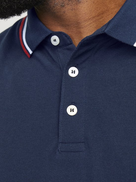 Donkerblauwe polo met rode en witte strepen aan kraag en mouwen, witte knopen.