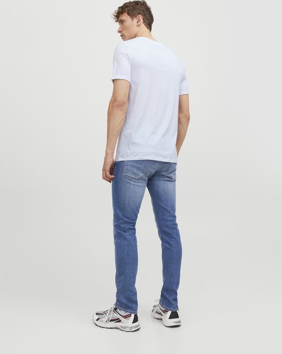 Man met witte T-shirt, blauwe jeans en sneakers, van achteren gezien.