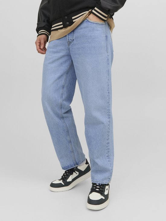 Man die een lichtblauwe loose fit jeans draagt met een beige vest en sneakers.