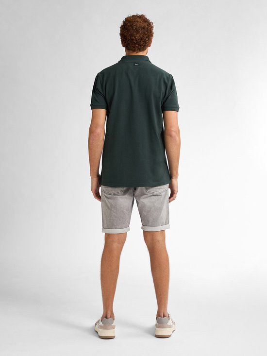 Man van achteren, draagt een donkergroene polo en een grijze denim short met opgerolde zomen. Hij draagt beige sneakers.