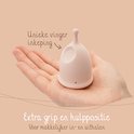Coupe menstruelle rose pâle avec encoche pour le doigt unique et grip supplémentaire pour faciliter l'insertion et le retrait, dans une main.