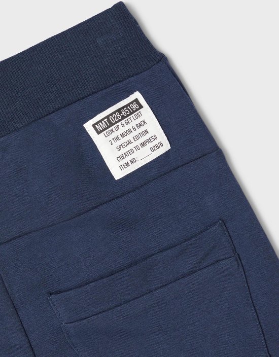 Detail van een donkerblauwe joggingbroek met een label met tekst en een achterzak.
