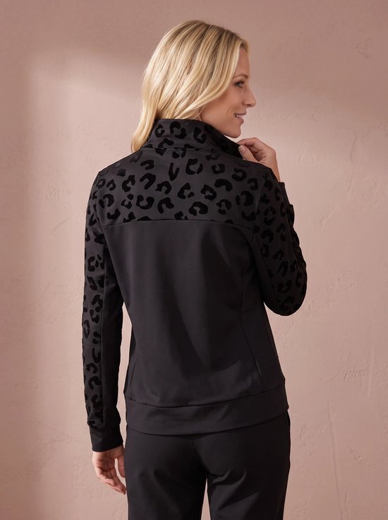 Model met blonde haren draagt een zwarte sportjas met zwarte panterprint op de rug en mouwen.